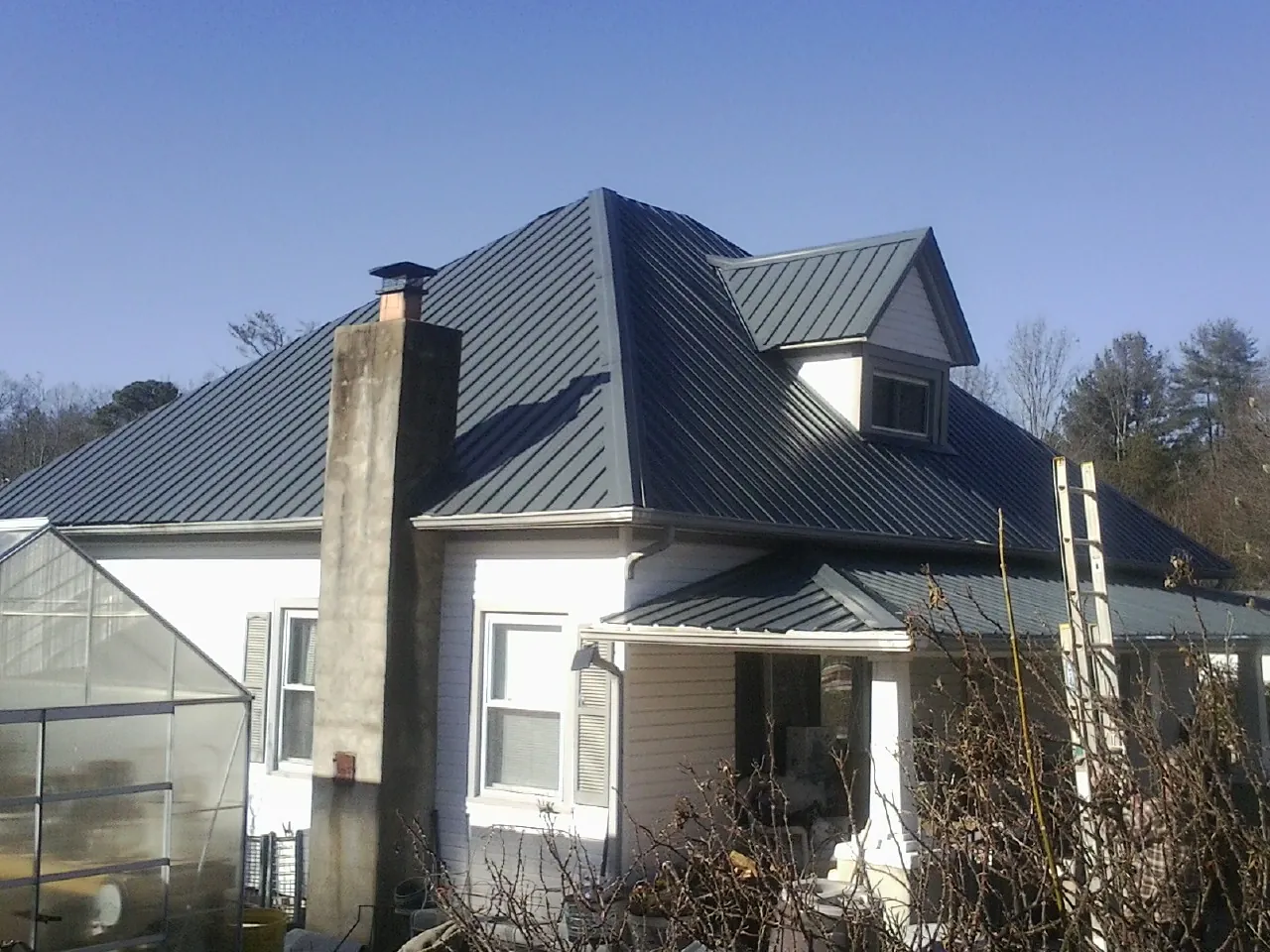 Dark blue standing seam metal roof on a white farmhouse with dormer — Slate & Tile Roof Repair by Roofing Brothers in Craigmont