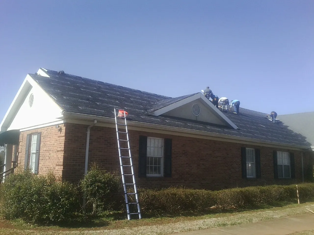 Crew tearing shingles off a brick ranch roof with a ladder set — Emergency Roof Repair work by our crew in Craigmont