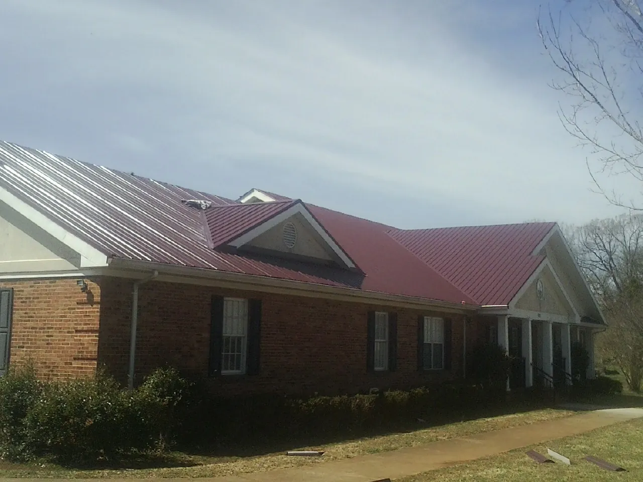 Red metal roof with gabled entries on a long brick building, from a Hail Damage Roof Repair job in Craigmont