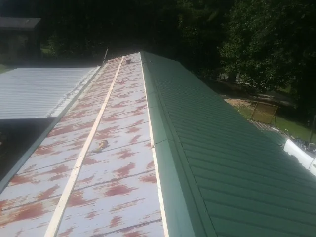 Old rusted panels beside newly installed green metal roofing — Wind Damage Roof Repair by Roofing Brothers in Craigmont