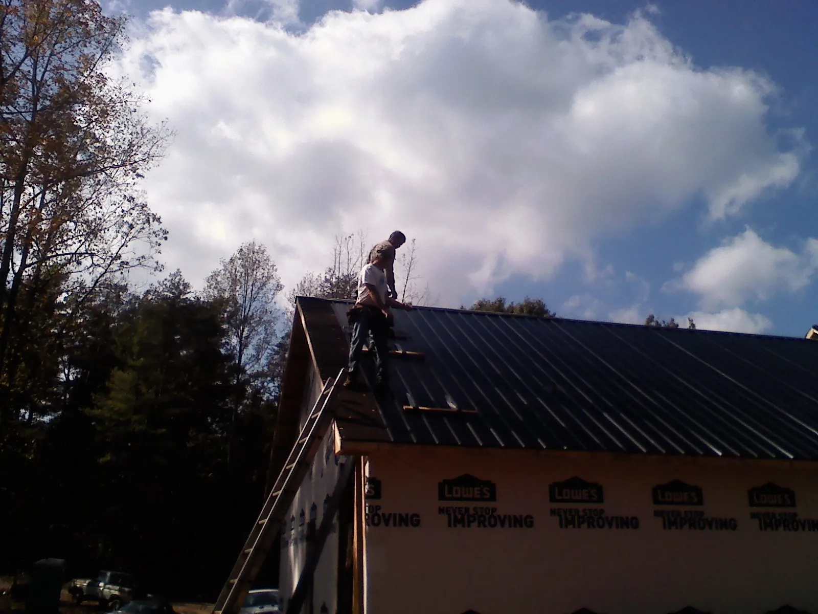 Roofer fastening dark metal panels high against a cloudy sky, from a Roof Inspection job in Craigmont