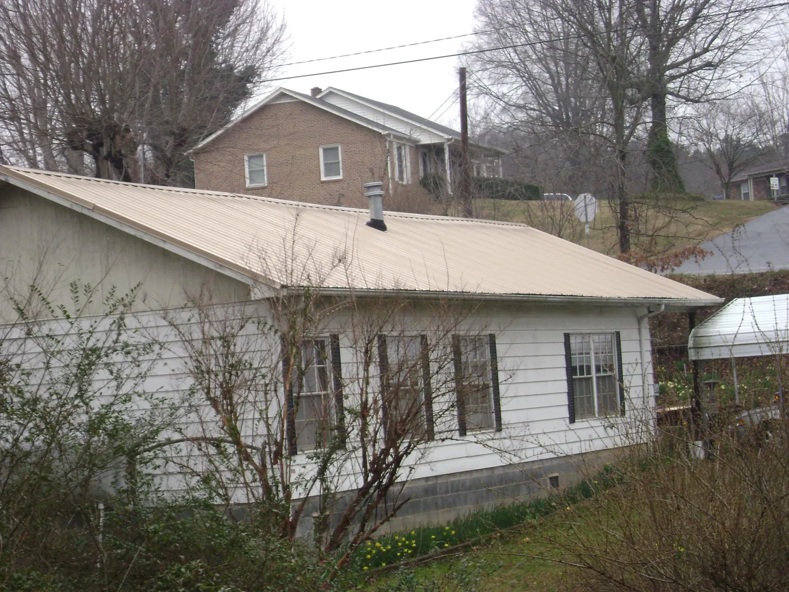 Tan metal roof on a white sided house set into a hillside — Commercial Roofing by Roofing Brothers in Craigmont