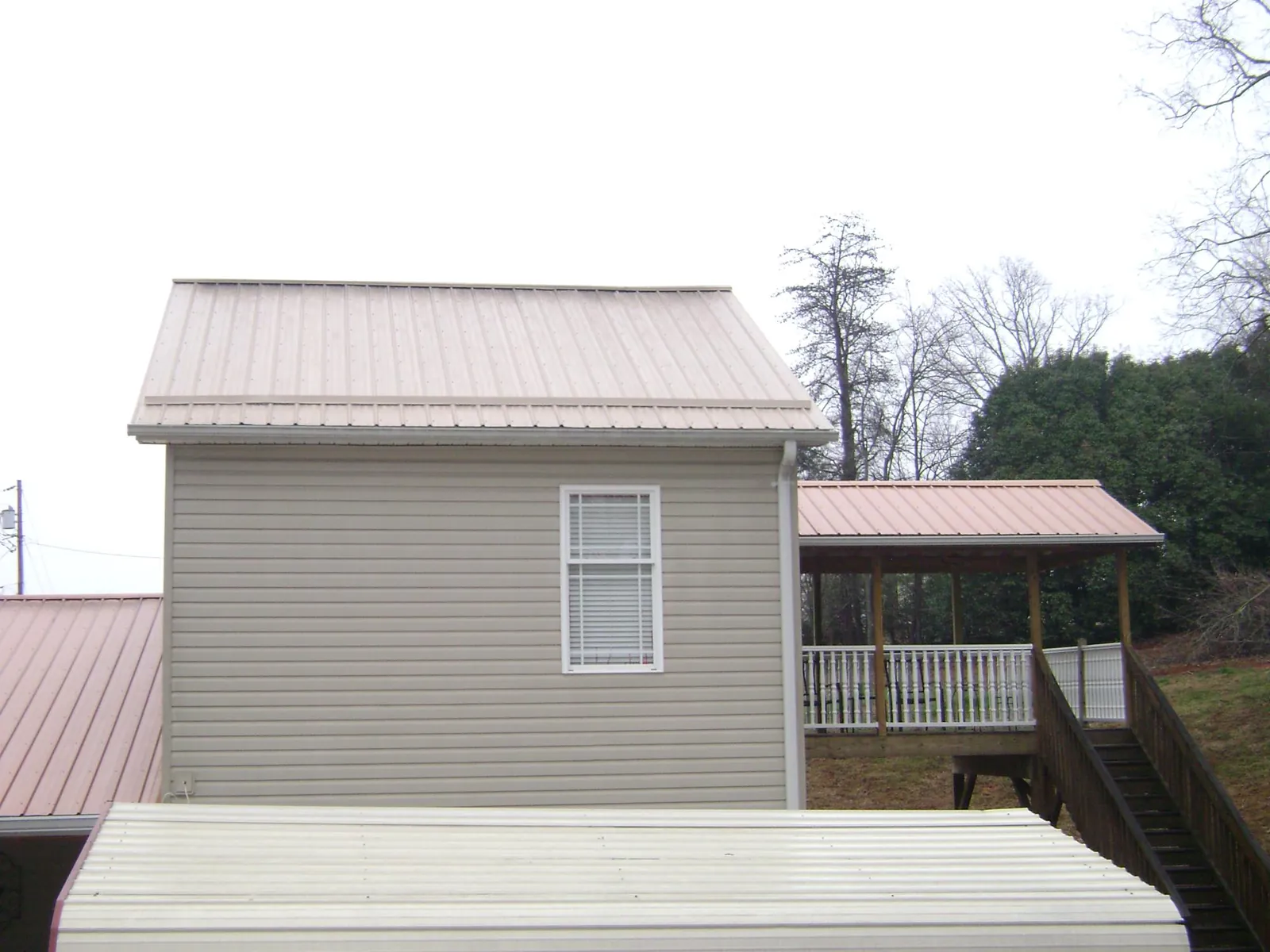 Tan metal roofs on a two story addition and attached porch, from a Roof Replacement job in Craigmont